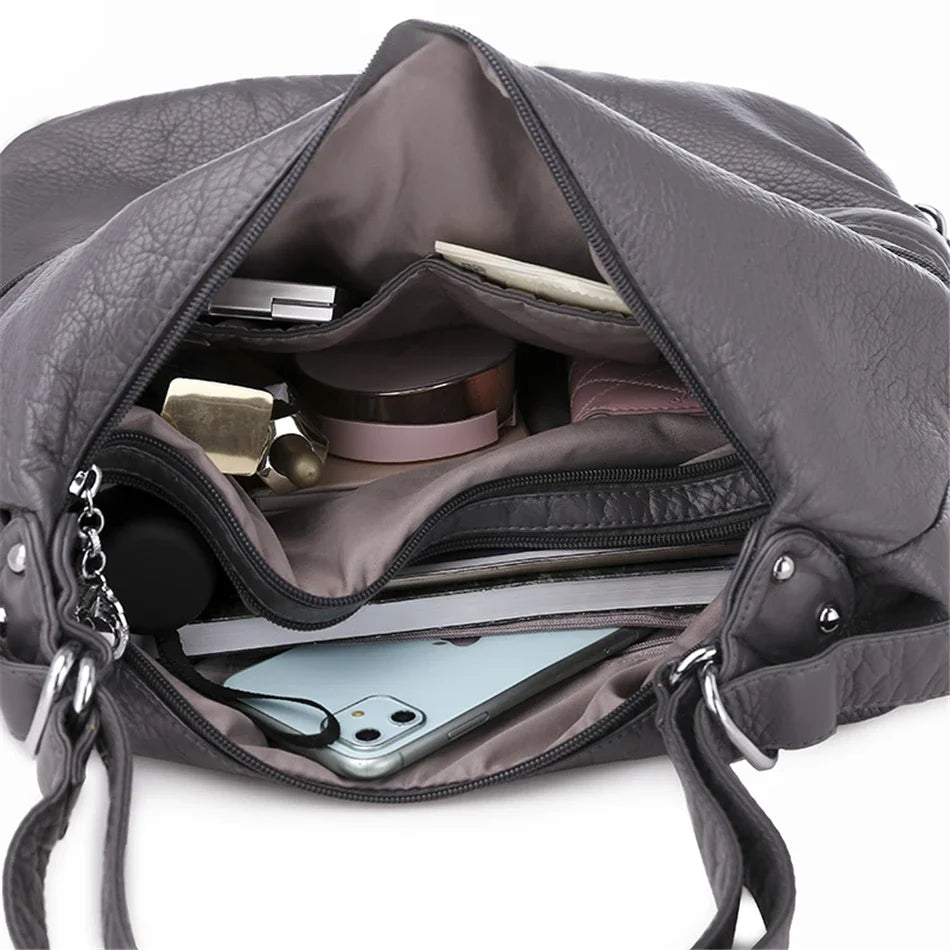 Vue intérieure d’un sac Vanderwah en cuir gris, montrant plusieurs compartiments organisés contenant un téléphone, du maquillage et des accessoires.