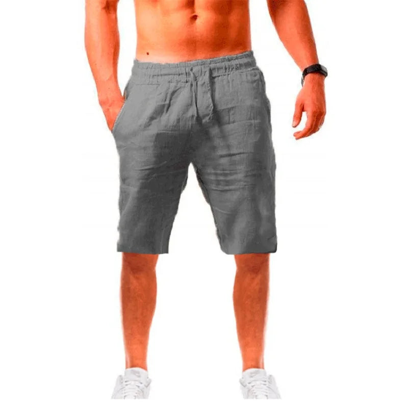 Homme élégant portant un short gris en lin ALTAREV, marchant près de la mer sur des escaliers blancs, ambiance estivale chic.