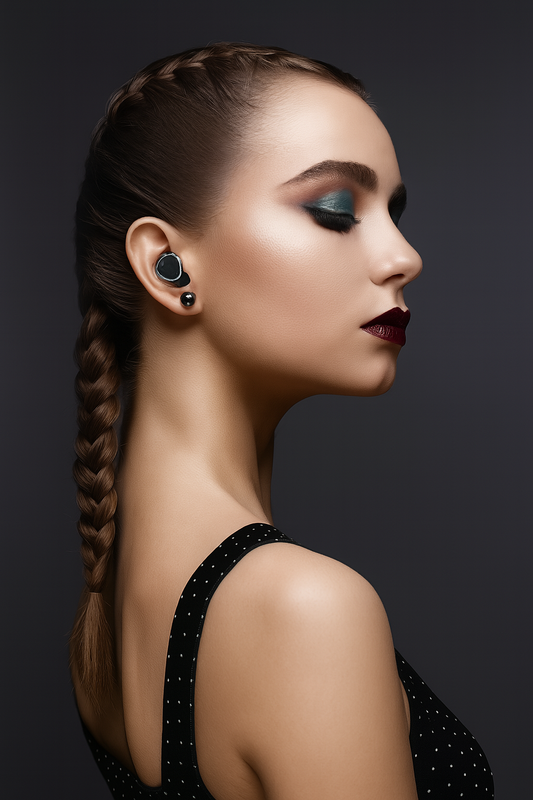 Portrait d’une femme élégante portant des écouteurs sans fil noirs au design moderne, sur fond sombre.