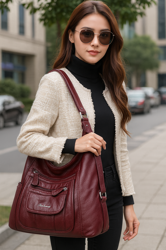 Femme élégante portant un sac à main en cuir bordeaux Vanderwah dans une rue urbaine, vêtue d’un col roulé noir et d’une veste beige.