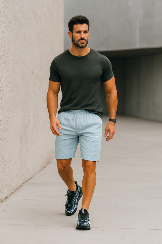 Homme musclé marchant en extérieur, vêtu d’un t-shirt noir, d’un short bleu clair et de baskets noires design ALTAREV.