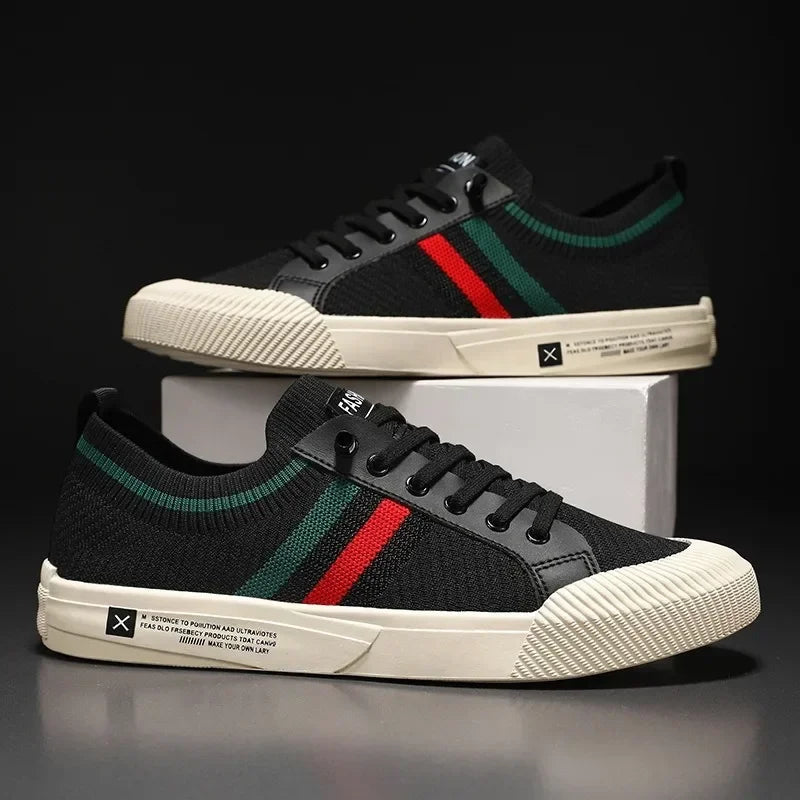 Chaussures sneakers noires pour homme posées sur socle, avec maille respirante et bandes rouge et vert, semelle blanche texturée.