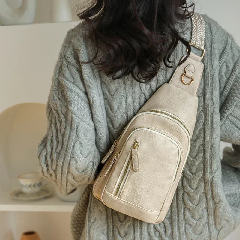 emme de dos portant un sac à bandoulière beige clair en cuir PU, assorti à un pull en maille torsadée gris, dans un décor intérieur doux et minimaliste.

