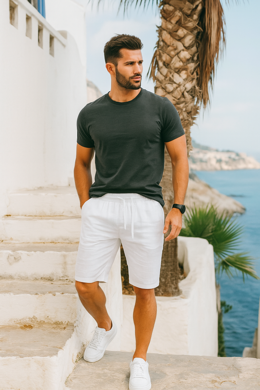 Homme élégant portant un short blanc en lin ALTAREV, marchant près de la mer sur des escaliers blancs, ambiance estivale chic.