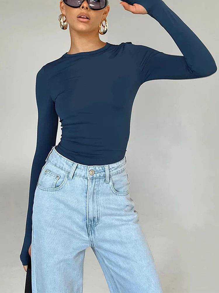 "Femme portant un haut moulant bleu marine à manches longues et un jean taille haute clair, accessoirisée de grandes boucles d'oreilles dorées et de lunettes de soleil noires."