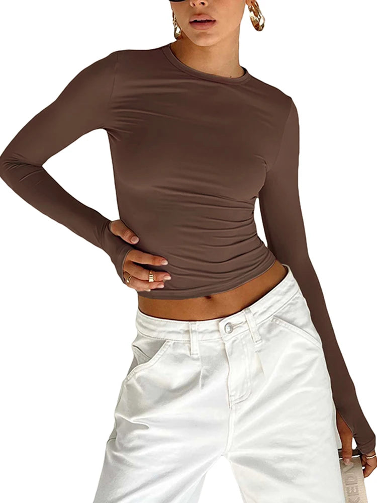 "Femme portant un top moulant marron à manches longues, coupe ajustée, avec un pantalon blanc taille haute et des boucles d’oreilles dorées."

