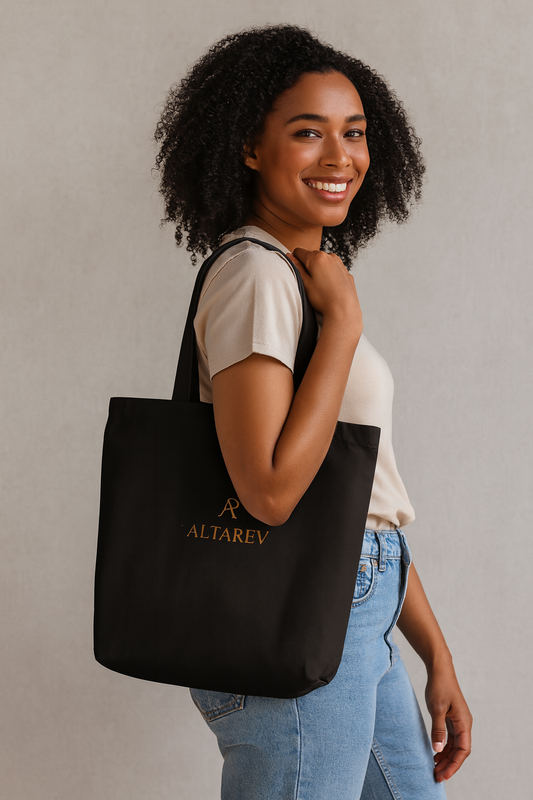 Femme souriante portant un tote bag noir ALTAREV avec logo doré, posant de profil contre un fond neutre, mettant en valeur l'élégance minimaliste du sac.