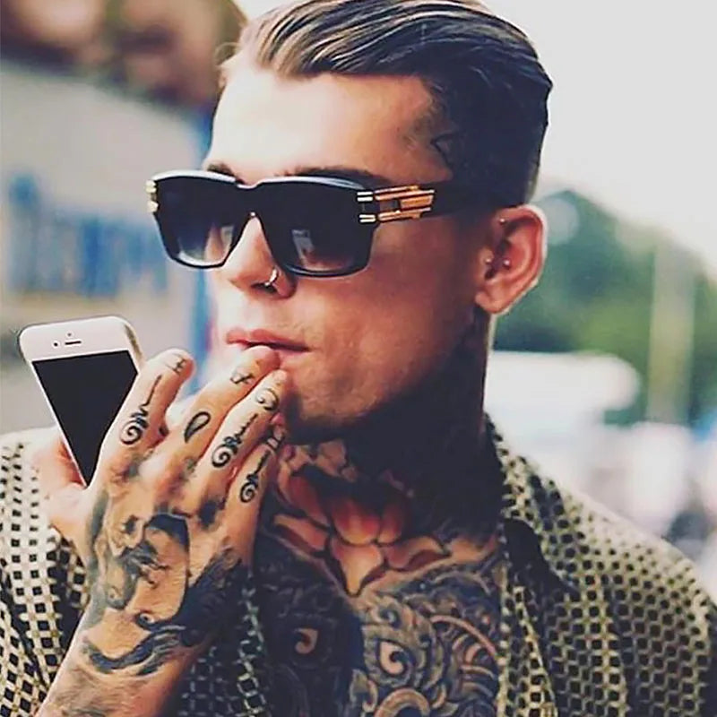 Homme tatoué portant des lunettes noires vintage avec branches dorées, style urbain luxueux.